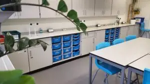 Close-up of storage and work area in a science classroom featuring blue drawer units, white cupboards, and integrated sinks.