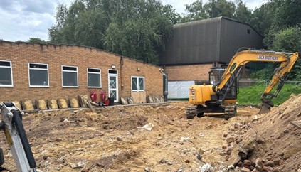 Education Services - Excavator at a construction site beside a brick building.