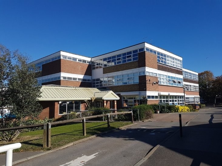 About - Exterior view of a multi-storey school building with large windows, modern brickwork, and landscaped surroundings.