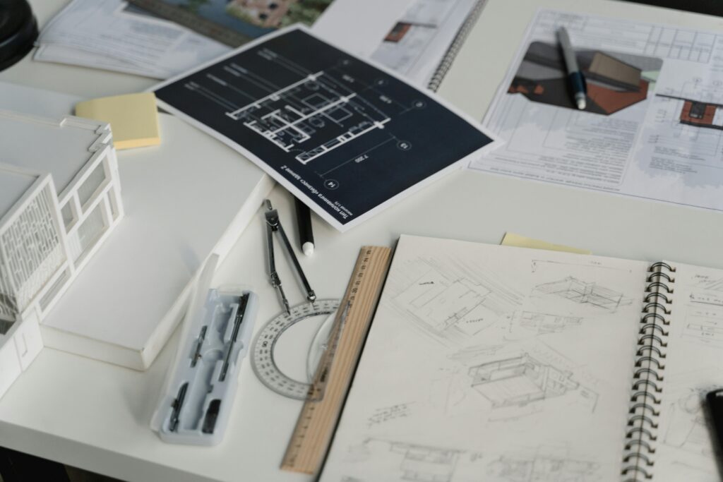Architectural design workspace with sketches, blueprints, scale models, and drafting tools laid out on a desk.