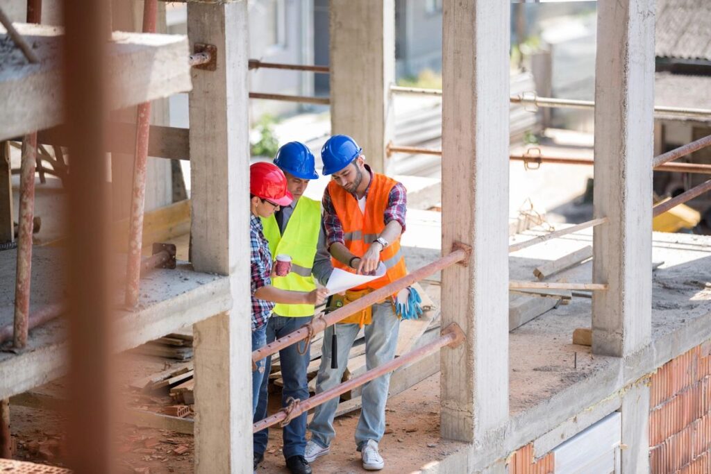 Construction workers and engineers reviewing tender documents on-site at a building project.