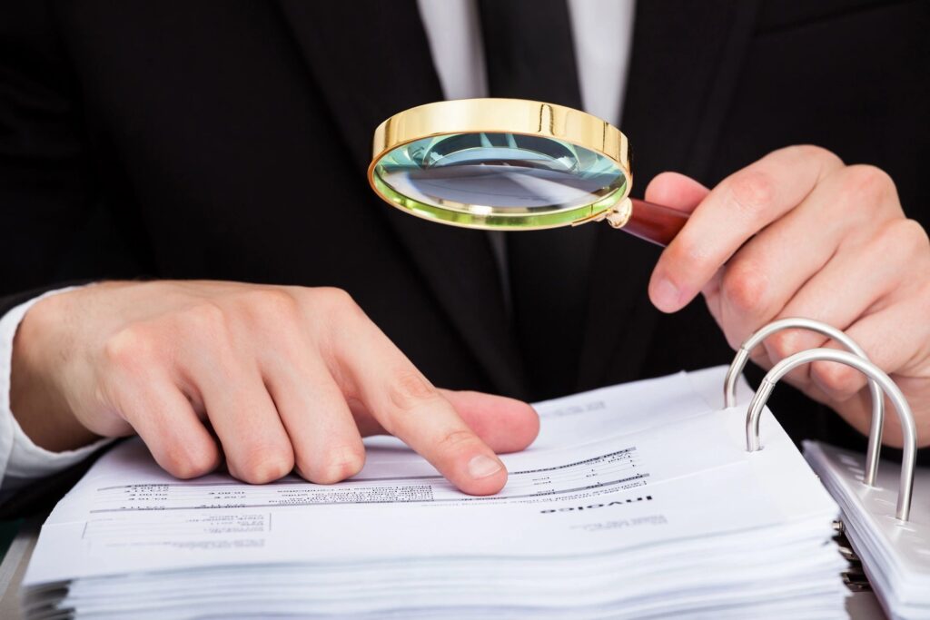 Business professional examining tender documents closely with a magnifying glass.