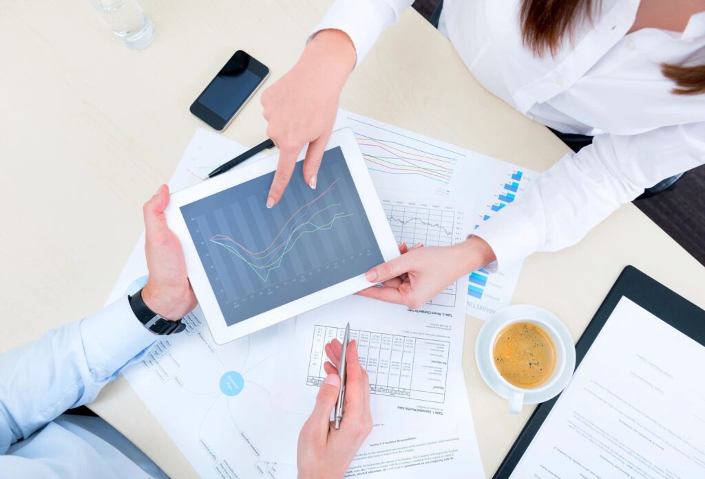 Urgent Capital Support Funding - Business professionals reviewing project delivery data and performance analysis on a tablet during a planning meeting.