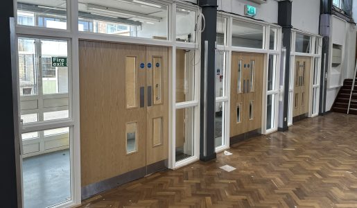 Newly installed wooden fire doors with vision panels in a school hall, enhancing safety and compliance.