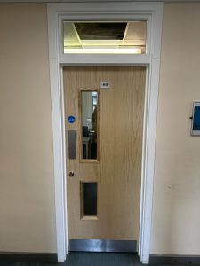Single wooden fire door with vision panels and safety compliance signage in a school corridor.