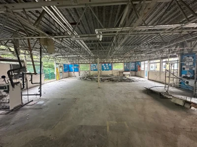 Interior of a partially demolished school building with exposed ceiling beams, removed flooring, and scattered debris, showing remnants of classroom walls and bulletin boards.