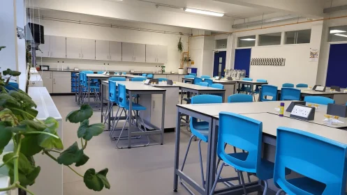 Wide view of a bright, spacious science lab with grouped student tables and blue chairs.