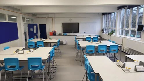 Front-facing view of a refurbished science classroom with natural light from full-length windows, digital board, and grouped desks.