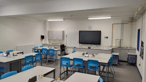 Wide-angle classroom view with multiple workstations, a large teaching screen, and integrated utilities for lab use.