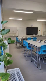 Interior of a completed science lab with blue chairs, grouped lab tables, and a digital teaching board at the front.