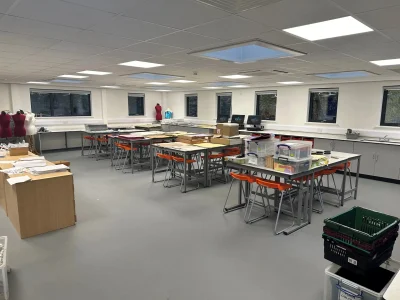 Modern classroom with grouped tables, orange stools, and mannequin forms, set up for design or textile work in a well-lit school environment.