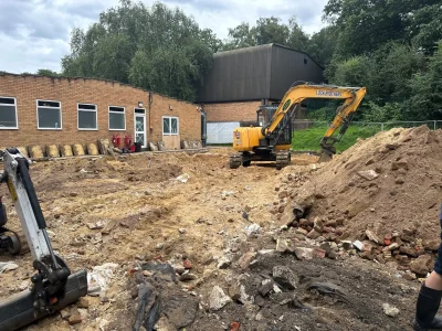 Construction site with excavators clearing debris and soil in front of a brick school building, preparing ground for new development.
