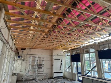 Interior classroom ceiling during construction, displaying new timber roof trusses and exposed services before insulation and ceiling installation.