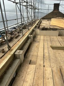 Roof construction site with timber decking and scaffolding in place, showing structural works in progress beneath protective sheeting.