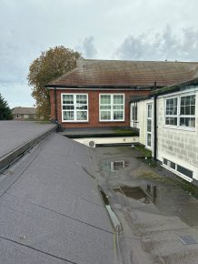 Knaphill - Case Study -Old flat school roof before refurbishment, showing worn red felt surface with visible cracks, patching, and poor drainage.