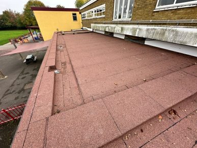Twydall Primary School - Newly installed red mineral felt flat roof on a school building, with visible drainage outlets and surrounding playground area.