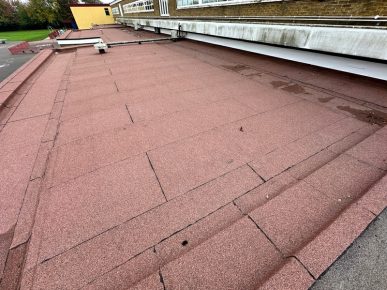 Newly installed red felt flat roof on a school building, featuring layered waterproofing and clean detailing near the parapet.