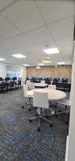 A classroom with computer desks around the walls and white circular tables in the middle of the room.