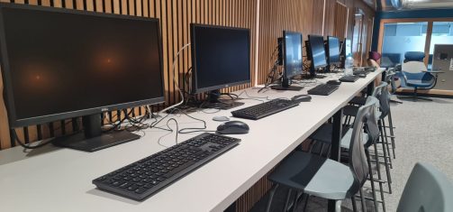 Close-up view of computer workstations arranged along a bench with stools.