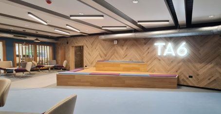 Sixth form common room with wood panelled walls, TA6 sign, and tiered seating for group study and presentations.